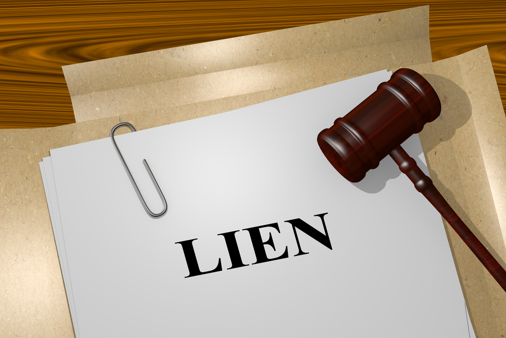 A stack of papers with the word 'Lien' on the top page, next to a judge's gavel on a wooden desk.