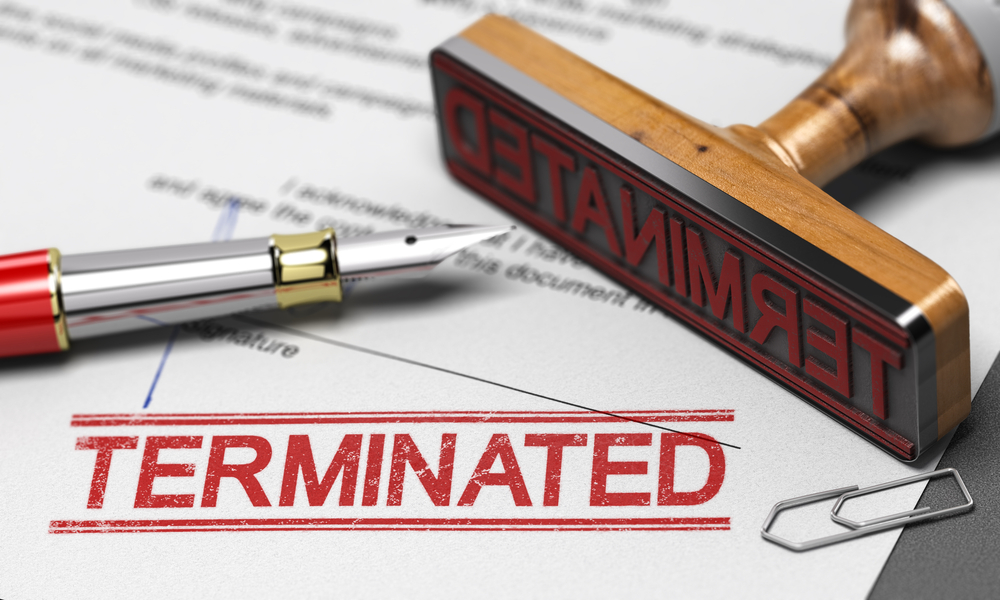 Rubber stamp marked "TERMINATED" on a document, with a fountain pen and paperclips nearby, symbolizing job or contract termination