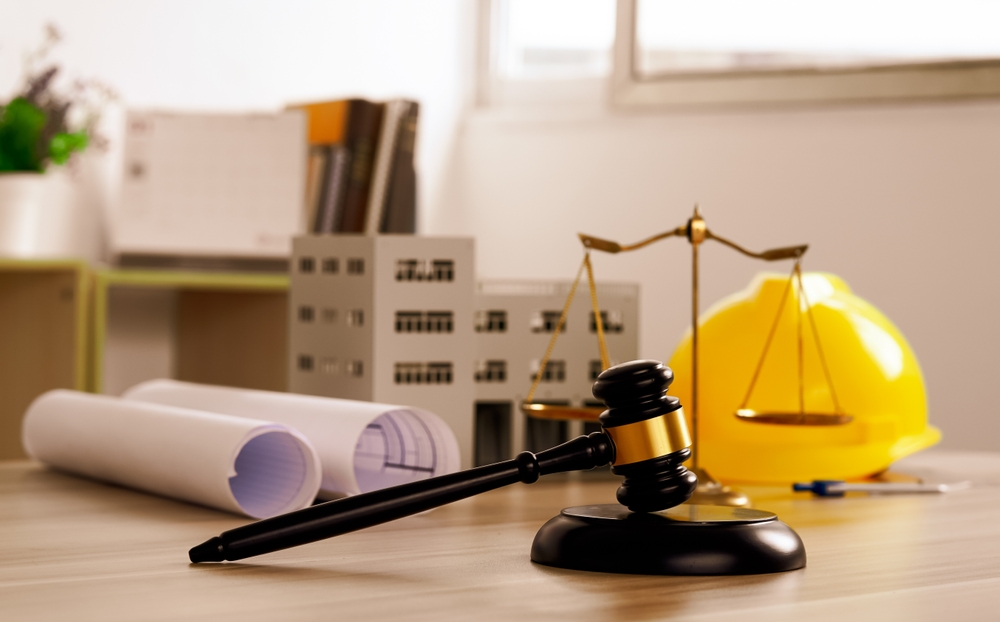 Gavel, scale, hard hat, and blueprints on a desk symbolizing construction law and legal planning
