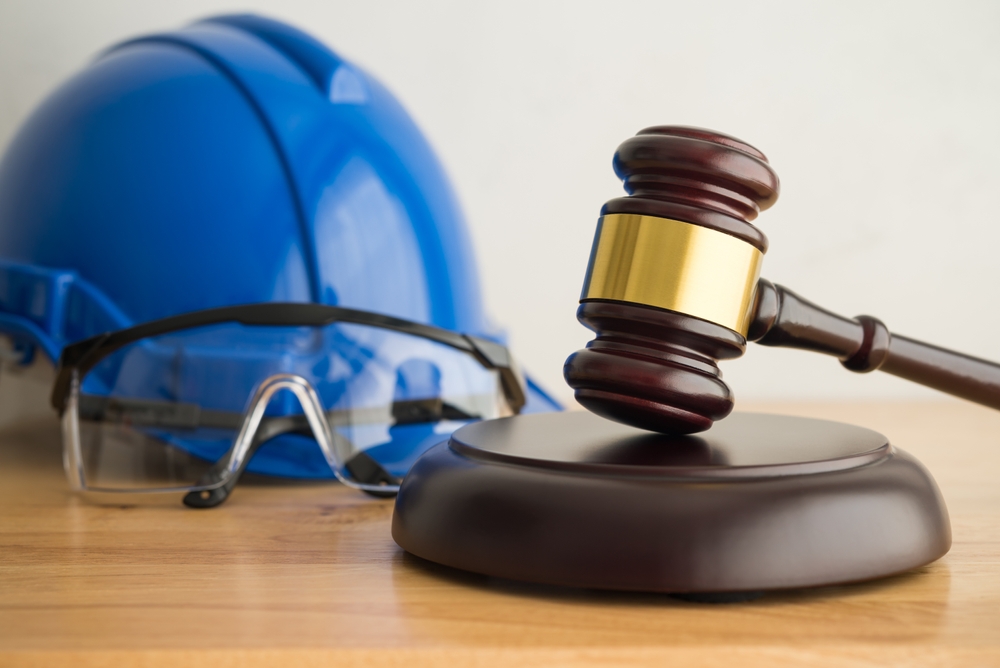 Wooden judge’s gavel resting near a blue safety helmet and clear protective glasses on a wooden surface
