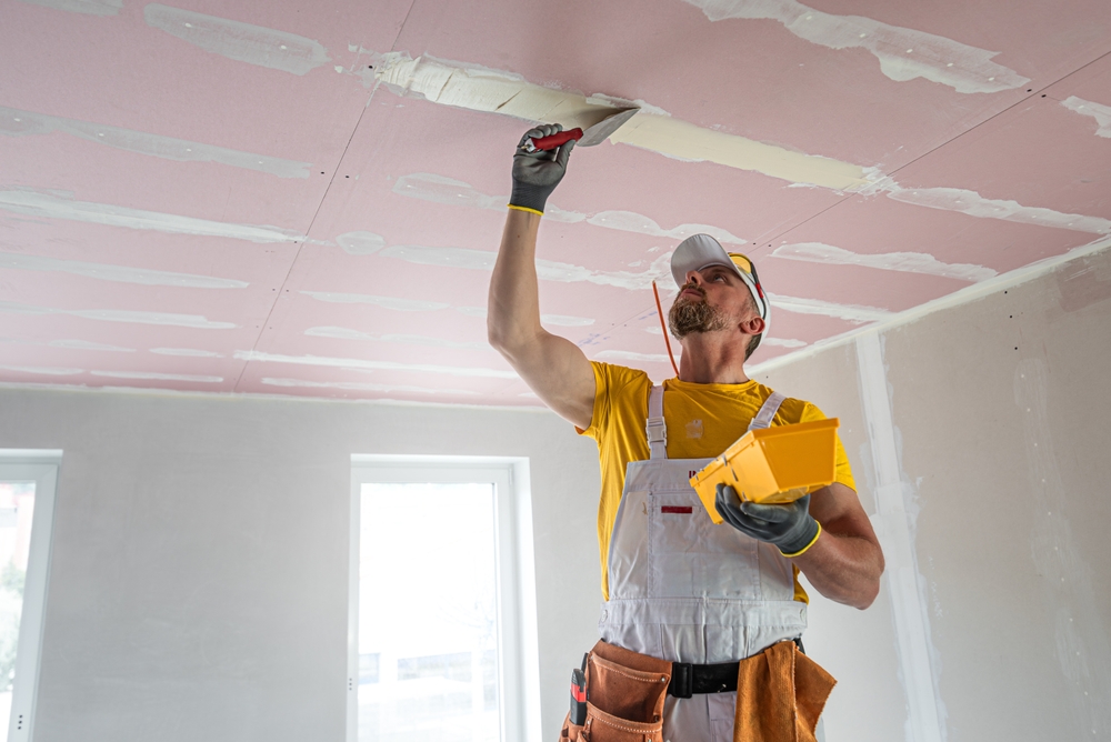 Man applying joint compound to a ceiling with a putty knife in a room under construction or renovation